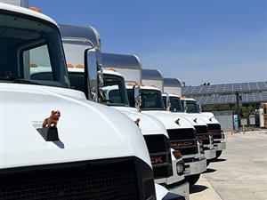 5 Cajon Valley MACK EV Trucks lined up in front of solar panels